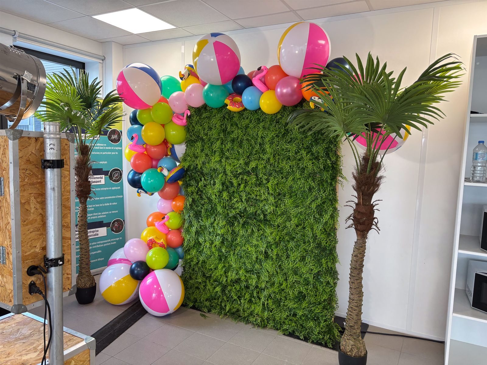 Décor tropical avec arche de ballons et mur végétal autour de la borne photo